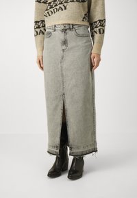 Jupe maxi en denim gris clair, avec une fente avant, un ourlet brut et un design classique à cinq poches. Associée à des bottines noires.