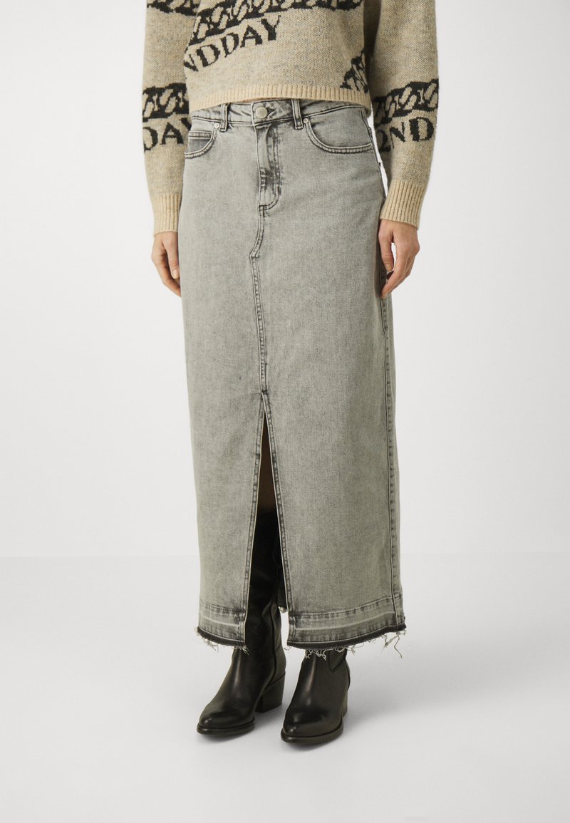 Jupe maxi en denim gris clair, avec une fente avant, un ourlet brut et un design classique à cinq poches. Associée à des bottines noires.