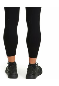 Leggings athletic neri con texture a coste, dotati di marcature a sinistra e a destra su entrambe le gambe inferiori. Abbinati a scarpe sportive nere.