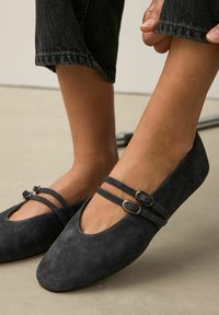 Zwarte suède balletschoenen met twee smalle bandjes en metalen gespen, afgeronde neuzen en een gladde, matte textuur.