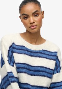 Gestrickter Pullover mit horizontalen Streifen in Marineblau und Hellblau auf cremefarbenem Hintergrund. Rundhalsausschnitt und lockere Passform.