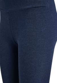 Granatowe dopasowane legginsy o gładkiej fakturze i wysokim pasie, pokazane od połowy uda do talii.