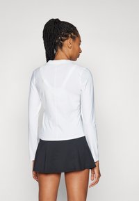 Top branco de manga comprida com textura suave, combinado com uma saia preta rodada. As costas apresentam um detalhe em costura e um decote arredondado.