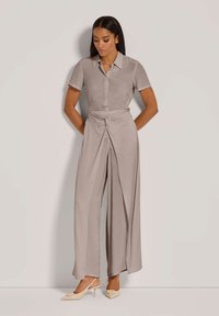 Licht beige, kortekleurige overhemd met knopen, gecombineerd met brede, gedrapeerde broek. De gladde textuur en de ontspannen pasvorm creëren een elegante silhouet.