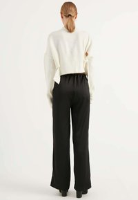 Witte gebreide cropped trui met open rugdetails, gecombineerd met zwarte wijde broek. Gladde textuur en neutraal kleurenpalet.
