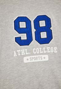 Szürke pulóver kék hímzett "98" számokkal és fehér szöveggel: "ATHL. COLLEGE SPORTS", sima felülettel.