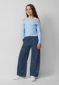 Hellblaues schulterfreies Oberteil mit weißem Blumenmuster, kombiniert mit locker sitzenden dunkelblauen Jeans und weißen Sneakers.