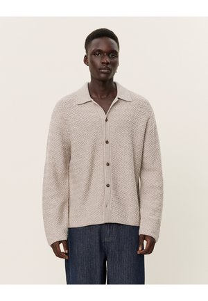 Beige teksturert cardigan med et subtilt sikksakkmønster, knapp foran og kragesnitt, sammen med mørkeblå vide bukser.