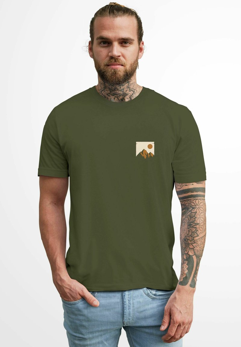 Olive green short-sleeve t-shirt with a chest pocket graphic featuring mountains and a sun in beige and orange colors. Cotton fabric, plain texture.