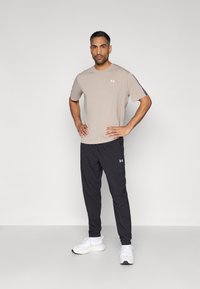 Ανοιχτό μπεζ κοντομάνικο πουκάμισο, μαύρο αθλητικό παντελόνι και λευκά αθλητικά παπούτσια, με λογότυπα στο πουκάμισο και το παντελόνι, ομαλή υφή.