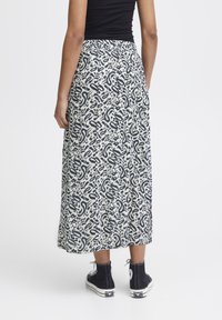 Lång, flödande kjol i krämfärgad med svart abstrakt mönster. Materialet verkar lätt; har en midjeresår och sidofickor. Matchas med svarta sneakers.