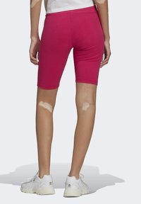 Dopasowane różowe prążkowane krótkie spodenki rowerowe o gładkiej teksturze, zestawione z białymi tenisówkami z subtelnym logo na pięcie.