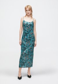 Duga teal haljina s cvjetnim uzorkom u crnoj i narančastoj boji. Ima tanke naramenice i ravni kroj suknje. Izrađena je od glatkog, teksturiranog materijala.