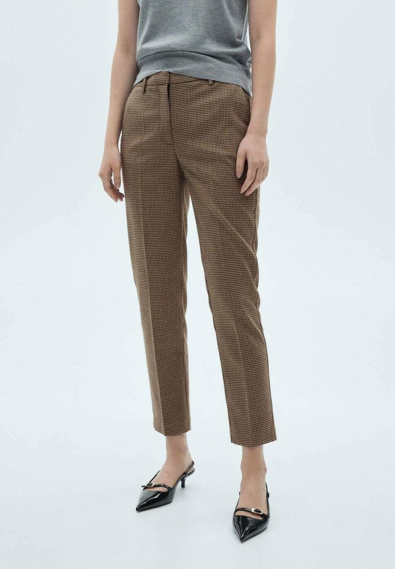 Pantalons à carreaux marron avec une coupe ajustée, présentants une taille mi-haute et une texture lisse. Associés à des talons aiguilles noirs.