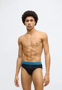 Fekete alsónadrág kék elasztikus derékpánttal, amelyen vastag betűkkel szerepel a "SCHIESSER" márkanév. Simább anyag és feszes illeszkedés.