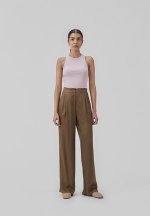 Lys pink ribbet tank top, højtaljede brune brede bukser, beige vævede slip-on sko, stående mod en ensfarvet grå baggrund.