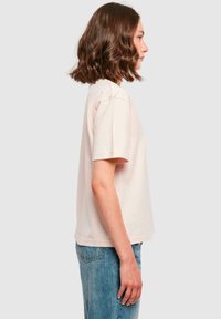 Lyserød bomulds t-shirt, korte ærmer, afslappet pasform, rund halsudskæring, vist på en person, parret med blå jeans. Enkel og udekoreret design.