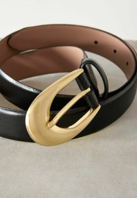 Zwarte leren riem met een grote, gouden metalen gesp met een gebogen ontwerp. De binnenkant is glad met een bruine afwerking; meerdere verstelgaten.
