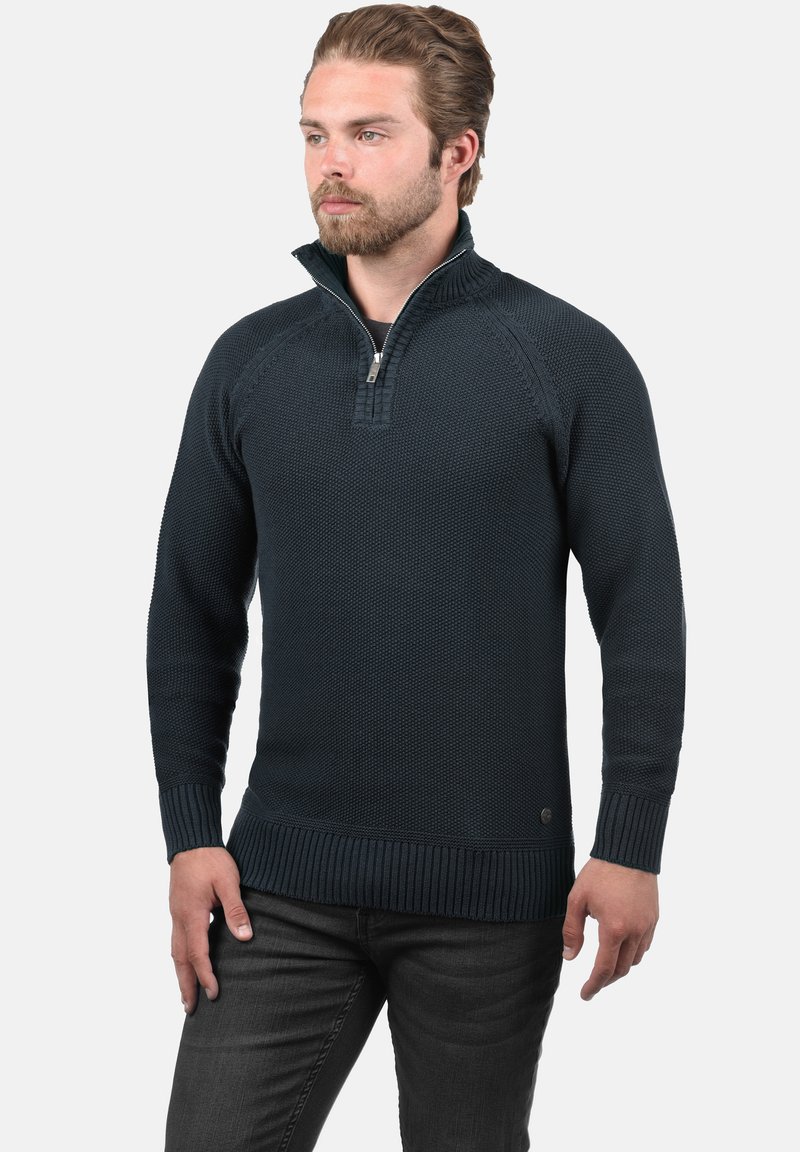 Suéter de punto azul marino con cuello con cremallera, puños y dobladillo acanalados, que presenta un patrón texturizado y un acento de logo en la parte inferior delantera.