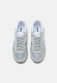 Pora šviesiai pilkų ir baltų Saucony Shadow sportbačių su tinklelio ir zomšos detalėmis, matoma iš viršaus ant balto fono.