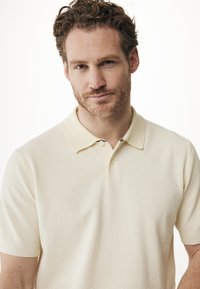 Kortärmad polo t-shirt i off-white, texturerat tyg med klassisk krage och två knappar, med subtila designaccenter vid halslinningen.