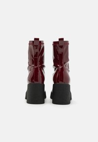 Botas de tobillo de charol burdeos con suela de plataforma negra texturizada, diseño fruncido y lengüetas en la parte posterior para facilitar el uso.