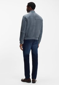 Giacca bomber in camoscio grigio con colletto e polsini a coste, caratterizzata da una texture liscia e un design leggermente aderente; abbinata a jeans in denim scuro.