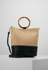 Borsa a secchiello in paglia naturale con base in pelle nera, dotata di un manico rotondo in bambù e di una tracolla regolabile.