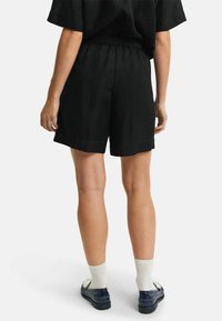 Zwarte linnen shorts met een elastische tailleband, met een relaxte pasvorm en gezoomde randen. Gecombineerd met marineblauwe schoenen en witte sokken.