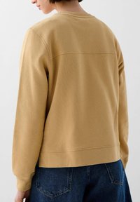 Mosterdkleurige sweatshirt met een ronde halslijn, lange mouwen en een rechte zoom. Structuurstof met een rugnaad-detail.