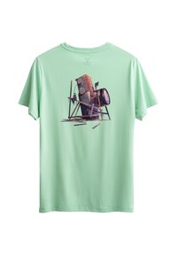 T-shirt vert clair avec un motif d'un appareil photo sur trépied, présentant une surface texturée et des formes géométriques dans un design minimaliste.