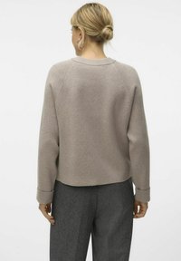 Hellgrauer Strickpullover mit einem cropped Design, Rippbündchen und -saum sowie Raglanärmeln. Getragen mit dunkelgrauen Hosen.