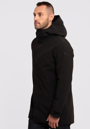 Veste à capuche noire avec une coupe droite, fermeture à pression et poignets en Velcro. Elle présente un tissu texturé et une patch logo sur la manche.