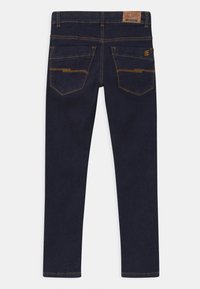 Jeans oscuros de corte Slim, con una cintura de altura media, bolsillos traseros con detalles de costura y una etiqueta de cuero en la parte trasera de la cintura.
