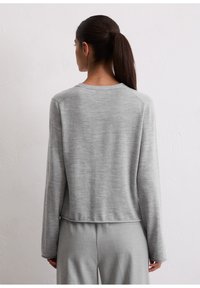 Maglione grigio in morbido tessuto; presenta maniche lunghe, un collo rotondo e una vestibilità leggermente accorciata, abbinato a pantaloni grigi coordinati.