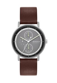 Montre argentée ronde avec un cadran gris, deux sous-cadrans, des accents verts et un bracelet en cuir brun. Présente un design minimaliste et des repères clairs.