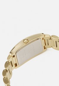Montre bracelet en métal doré avec un boîtier rectangulaire, finition texturée et bracelet en maillon en acier inoxydable. Dispose d'une couronne sur le côté et d'un dos gravé.