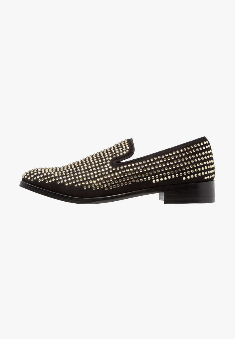 Chaussure noire à enfiler avec un petit talon, recouverte de petits clous dorés ronds, espacés uniformément, vue de côté extérieur.