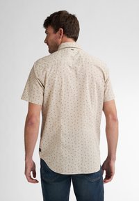 Beige overhemd met korte mouwen en een licht patroon van bordeauxrode stippen, voorzien van een rechte kraag en een rechte onderkant, gecombineerd met donkere jeans.