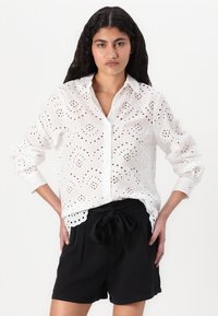 Hvit broderie anglaise skjorte med lange ermer, med knappestolpe foran og hullmønster. Kombinert med svarte shorts med snøring.