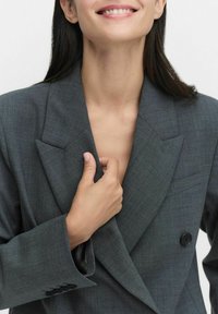 Grå blazer med en strukturerad design, dubbelknäppt stängning och breda slag. Har en smidig textur och en enkel bröstficka.