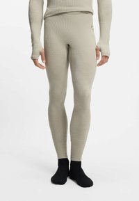 Jasnobeżowe termiczne legginsy o prążkowanej fakturze. Charakterystyczny dopasowany krój oraz otwory na kciuki w rękawach, zestawione z czarnymi skarpetami.