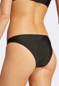 Černé bikiny s hladkým, pružným materiálem. Mají nízký střih s minimálním zakrytím a jemným logem.