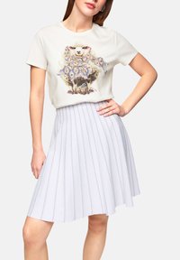 Light cream t-shirt with a sheep graphic, paired with a pleated light gray skirt featuring vertical stripes and subtle shimmer.