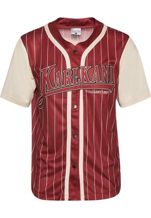 Sarkans un krēms kreklis ar vertikālām svītrām, ar pogu priekšpusi un logo uz krūtīm. Izgatavots no gludas auduma ar mīkstu tekstūru.