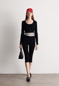 Crni dugosavljeni top i tajice upareni s crvenom kapom i crnom torbicom. Outfit sadrži bijeli pojas u akcentu i ravne cipele.