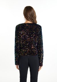 Crni top s dugim rukavima ukrašen šarenim sequinom i okruglim izrezom, uparen s crnim hlačama. Glatka tekstura.