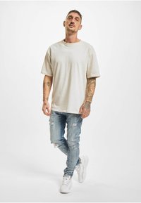 Beige oversized t-skjorte med kort erme, kombinert med lyseblå slitte jeans. Fottøy inkluderer hvite sportssneakers.