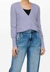 Ljuslila ribbad cardigan med djup V-hals, knappstängning och långa ärmar, tillsammans med slitna blå denimjeans.