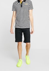 Mustavalkoraidallinen pikeepaita keltaisella aksentilla, yhdistetty mustiin shortseihin ja kirkkaan keltaisiin tennareihin, jossa on klassinen kaulussuunnittelu.